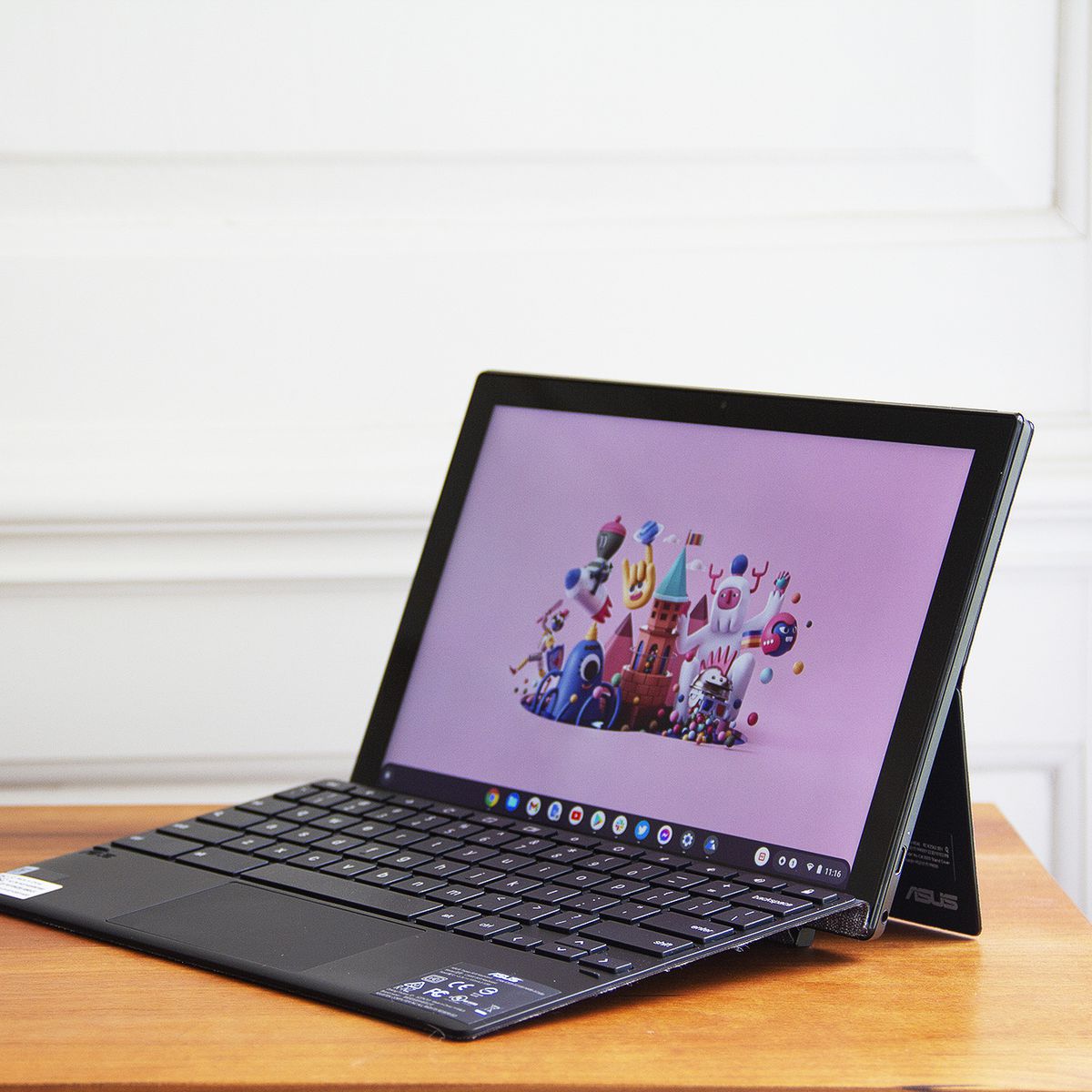 The Asus Chromebook Detachable CM3 open, angled to the left. The screen displays a cartoon city scene on a pink background.