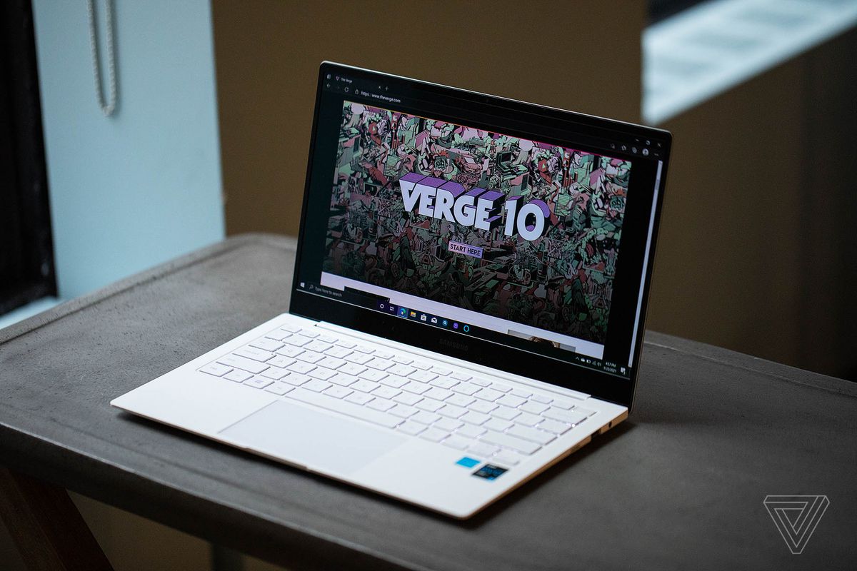 The Samsung Galaxy Book Pro 13 open seen from above and to the right on a brown table. The screen displays a Verge 10 graphic.