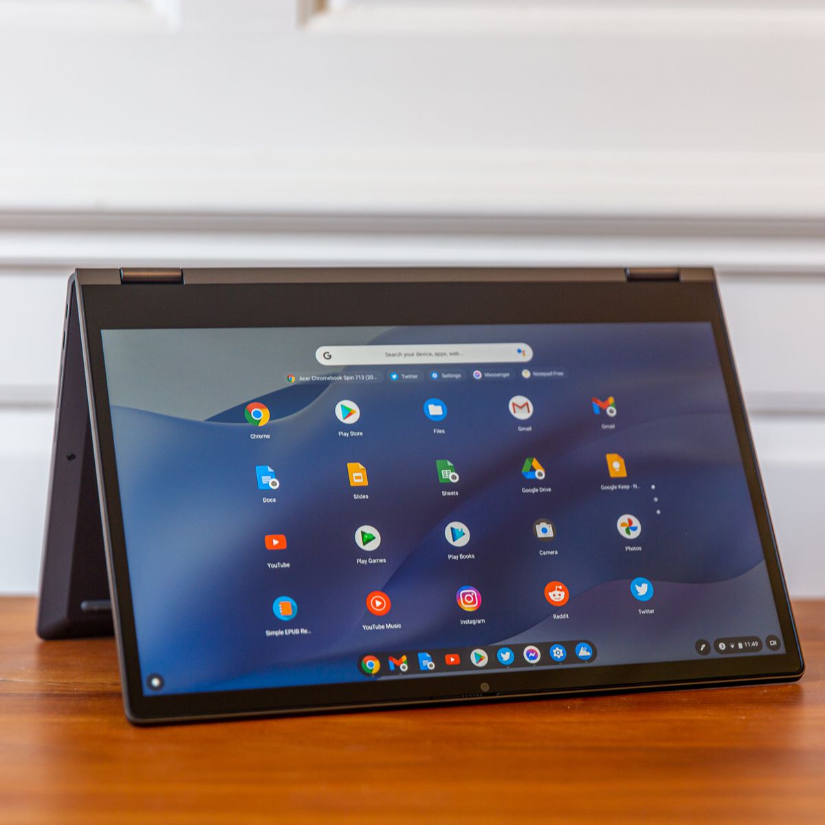 The Lenovo Flex 5 Chromebook in tent mode, angled to the right. The screen displays a grid of Chrome OS apps on a blue wavy background.