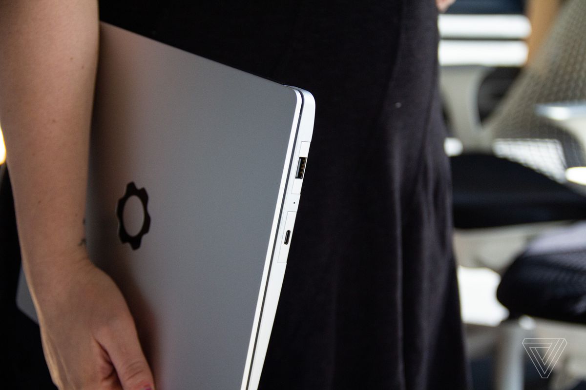 A user holds the Framework laptop beneath their arm in an office setting with the lid visible.