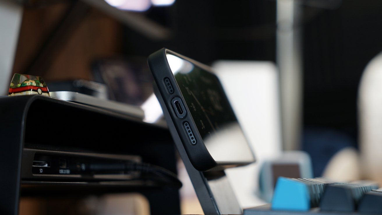 An iPhone 15 Pro Max in a Torras case on a MagSafe stand behind a keyboard on a desk