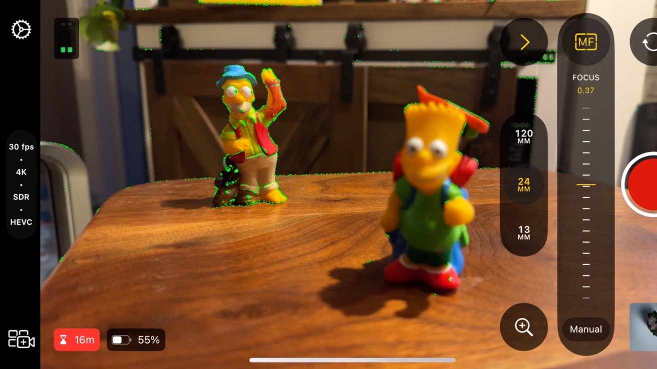 A screenshot from the Final Cut Camera app that shows two plastic figures from The Simpsons, one close and one far. The far one is in focus with green highlights around the edges showing the focus peaking setting