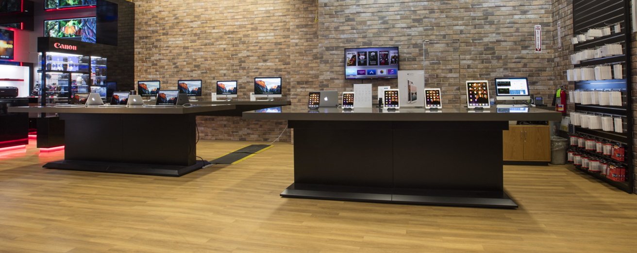 Adorama store in NYC showcasing Apple laptops and tablets on two large tables, with brick walls and wooden flooring.