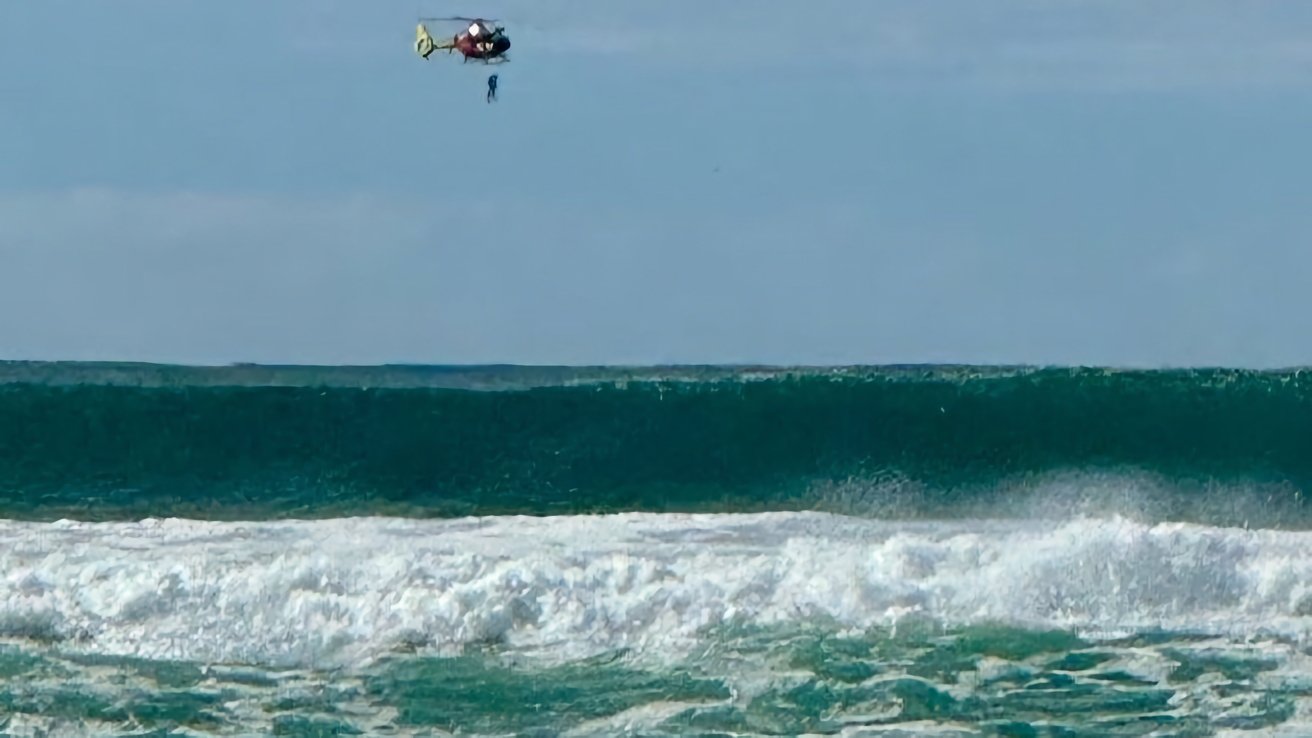 A helicopter hovers above the ocean, performing a rescue operation amid large waves.