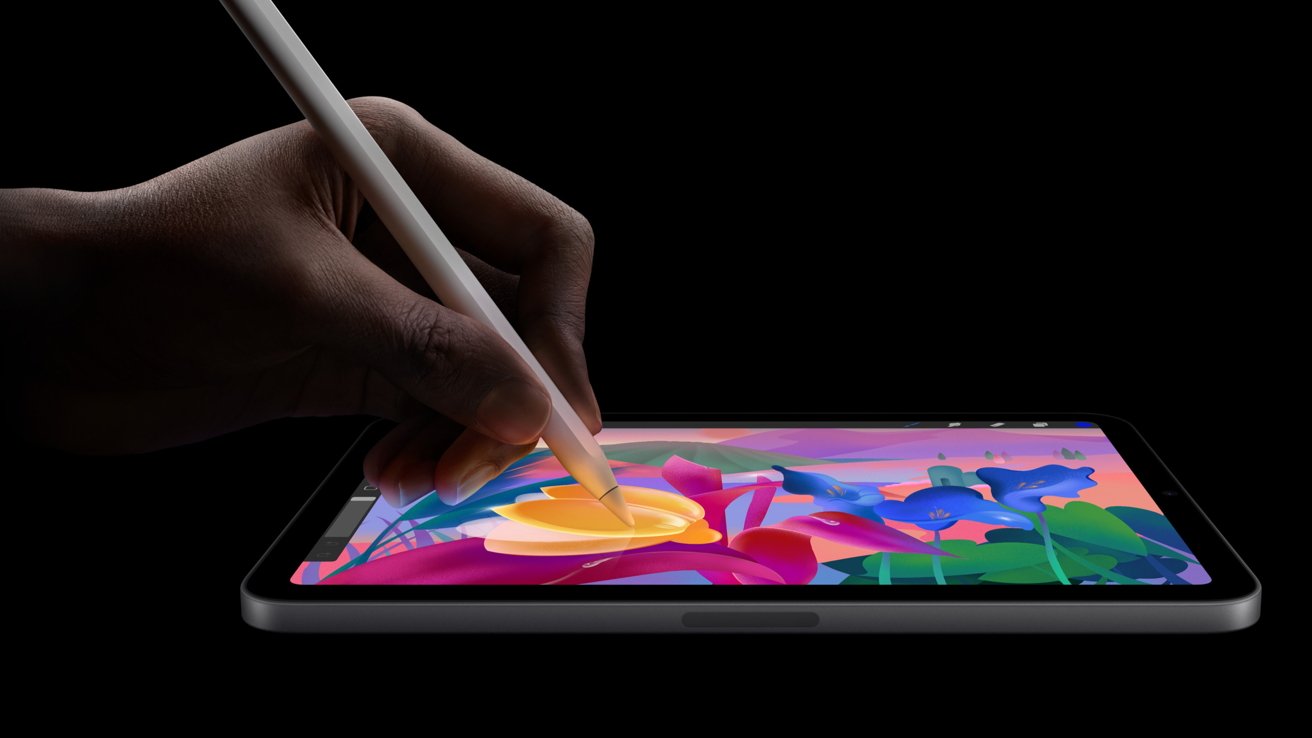 Hand using a stylus to draw colorful flowers on a tablet screen against a black background.