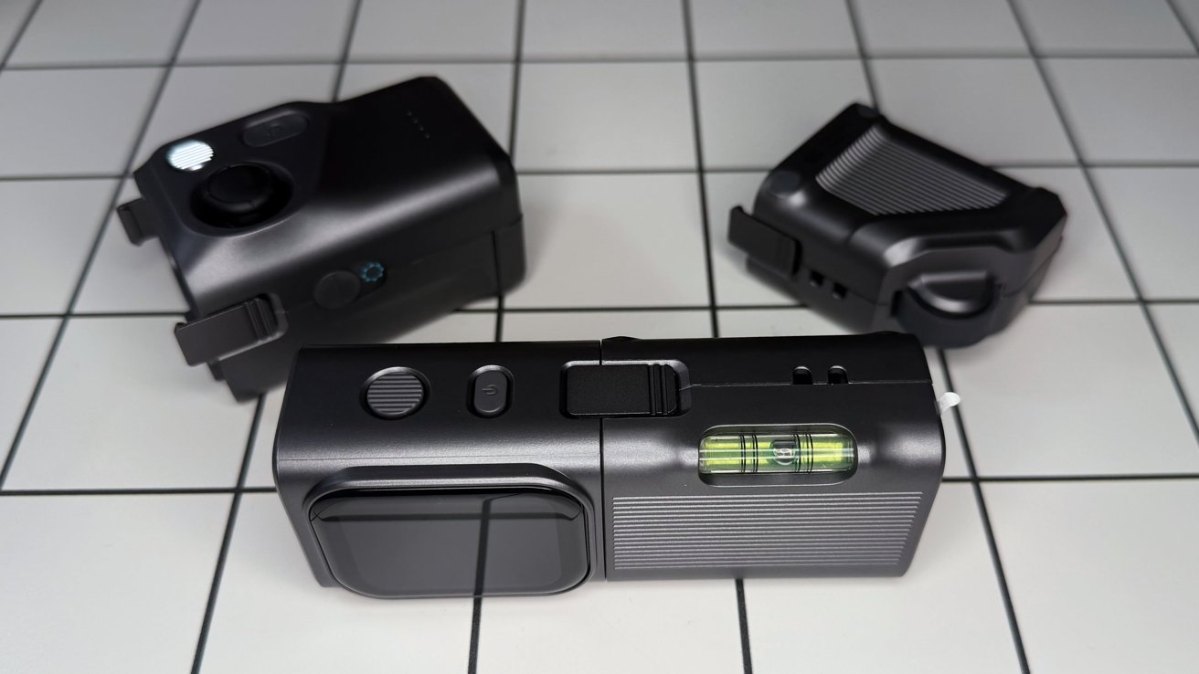 Three black camera-like devices on a tiled surface, each with various buttons and features, including a bubble level on one.