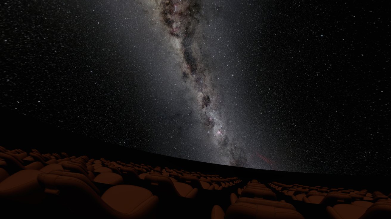 Planetarium interior with rows of empty seats facing an overhead projection of the Milky Way galaxy, surrounded by a star-filled sky.