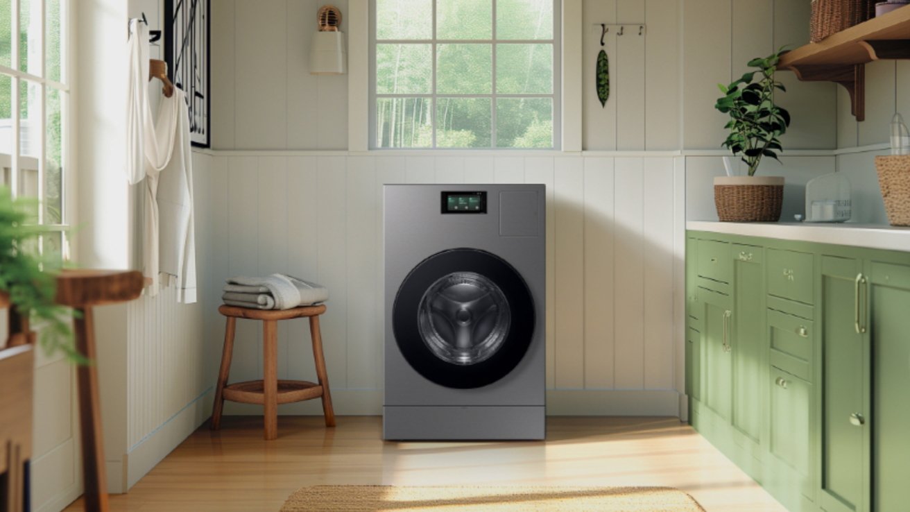 Cozy laundry room with a front-loading washing machine, green cabinets, wooden stool with folded towels, hanging shirt, potted plant, and sunlight streaming through the window.